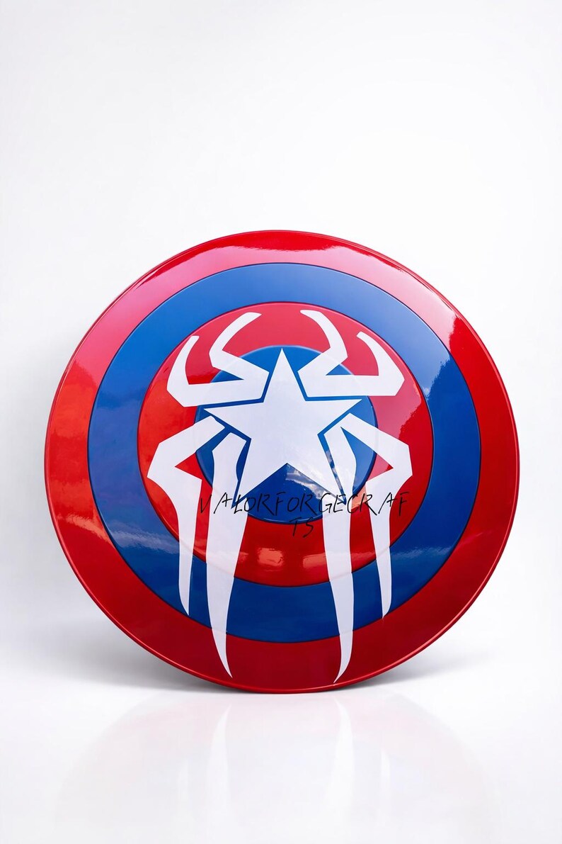 May include: A red, white, and blue shield with a star and spider-like design. The shield has a glossy finish and the text "VALOR FOR GECRAF 13" is written on it. The shield is a prop or collectible.