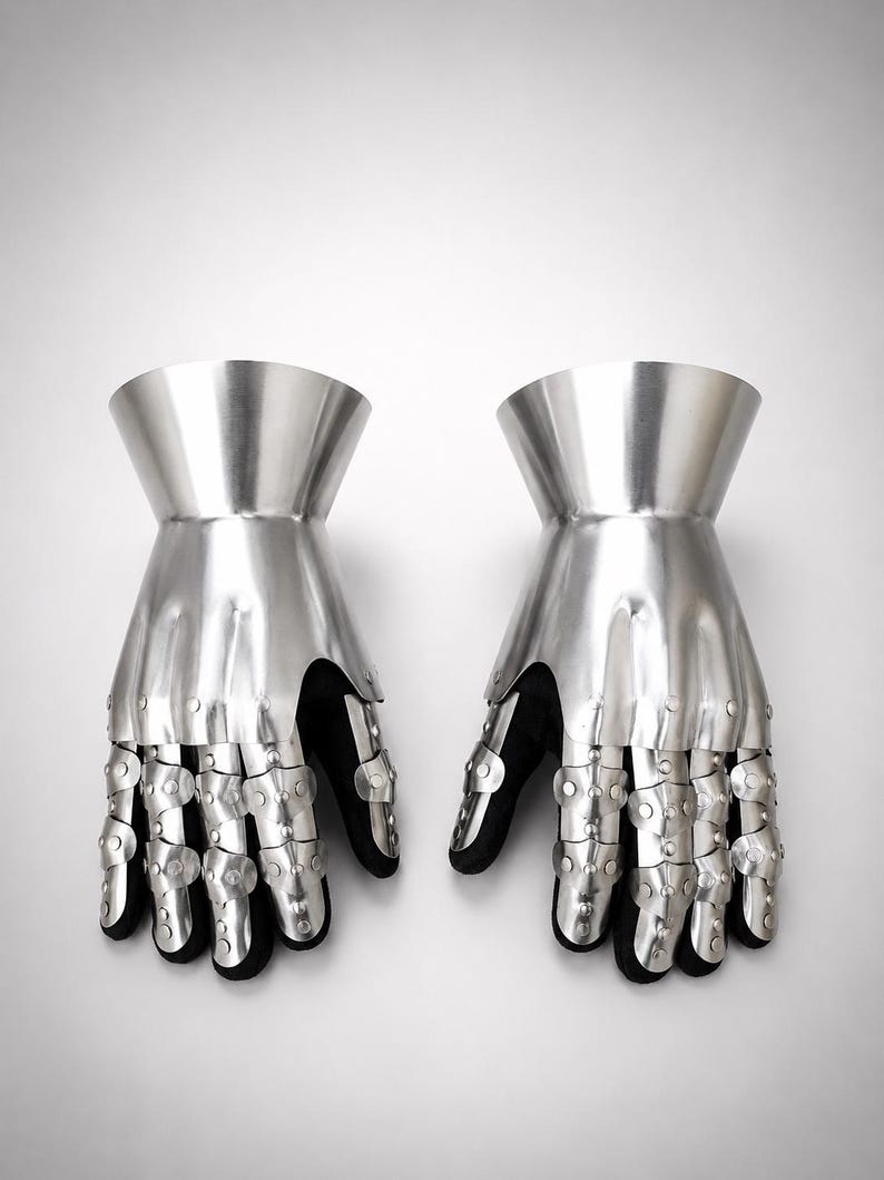 May include: A pair of articulated metal gauntlets featuring a polished silver finish. Each gauntlet consists of a flared cuff, a solid hand plate, and segmented finger coverings connected by rivets, all mounted over a black fabric base.