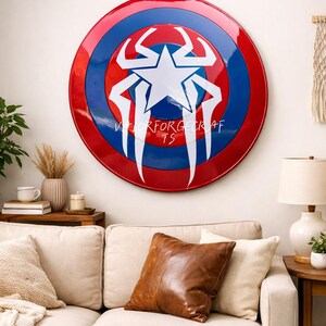 May include: A large, round shield with a red outer ring, blue inner ring, and a white star and stylized design in the center. The text "VALORFORGECRAFT TS" is printed on the shield. The shield is hanging on a white wall.