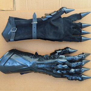May include: A pair of black gauntlet gloves. One glove is made of black suede with adjustable leather straps and metal buckles. The other glove is constructed from black molded material with articulated finger plates and sharp, pointed metal claw tips.