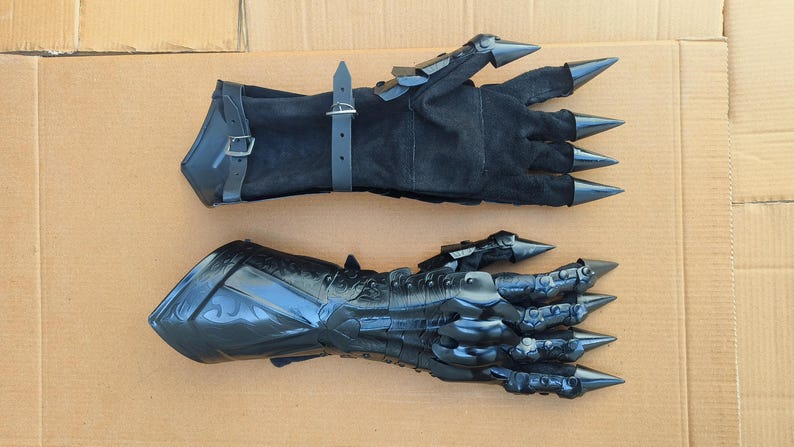 May include: A pair of black gauntlet gloves. One glove is made of black suede with adjustable leather straps and metal buckles. The other glove is constructed from black molded material with articulated finger plates and sharp, pointed metal claw tips.