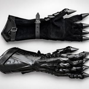 May include: A pair of black gauntlets featuring a combination of soft suede-like material and rigid, polished black metal plating. The design includes articulated finger sections topped with sharp, conical spikes and adjustable leather buckle straps.