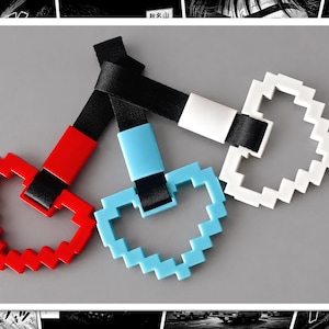 May include: Three pixelated heart-shaped car accessories in red, light blue, and white. Each heart is attached to a black strap. The items are displayed on a gray background.