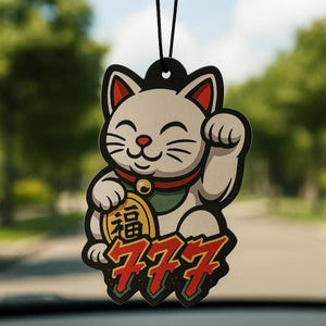May include: A hanging car air freshener featuring a cartoon beckoning cat with white fur, red ears, and a green collar with a gold bell. The cat holds a gold coin with the Chinese character for fortune, and the text 777 is printed in red below.