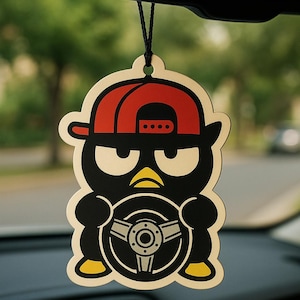 May include: A car air freshener shaped like a cartoon penguin wearing a red baseball cap and holding a steering wheel. The penguin is black with yellow accents and white eyes. The air freshener hangs from a black string.