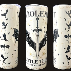 Op de afbeelding: Een witte beker met een zwart en goud design. Het ontwerp bevat vleermuizen, sterren en de tekst "VIOLENT LITTLE THING I WILL NOT DIE TODAY" met een zwaard en vleermuisvleugels. De beker heeft een zilveren deksel.