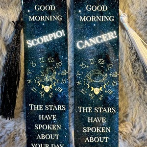 May include: Two rectangular bookmarks with a starry night sky design. One bookmark says "Good Morning Scorpio!" and the other says "Good Morning Cancer!". Both bookmarks have the text "The stars have spoken about your day."