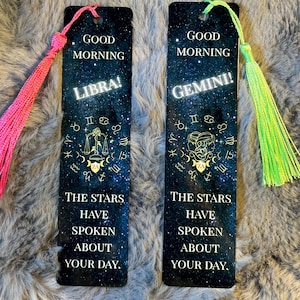 May include: Two rectangular bookmarks with a starry night sky design. One says "Good Morning Libra!" and the other says "Good Morning Gemini!" Both have a tassel at the top and the text "The stars have spoken about your day."