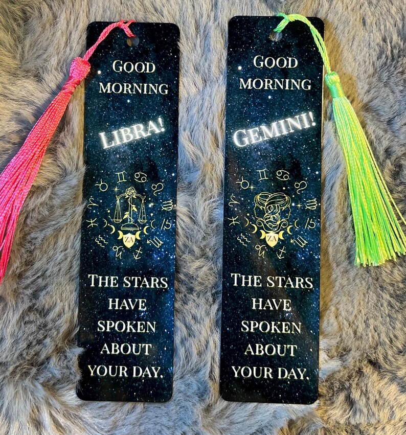 May include: Two rectangular bookmarks with a starry night sky design. One says "Good Morning Libra!" and the other says "Good Morning Gemini!" Both have a tassel at the top and the text "The stars have spoken about your day."