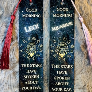May include: Two rectangular bookmarks with a starry night design. One features "Leo!" and a lion symbol, the other "Aquarius!" and a water bearer symbol. Both have the text "Good Morning" and "The stars have spoken about your day."