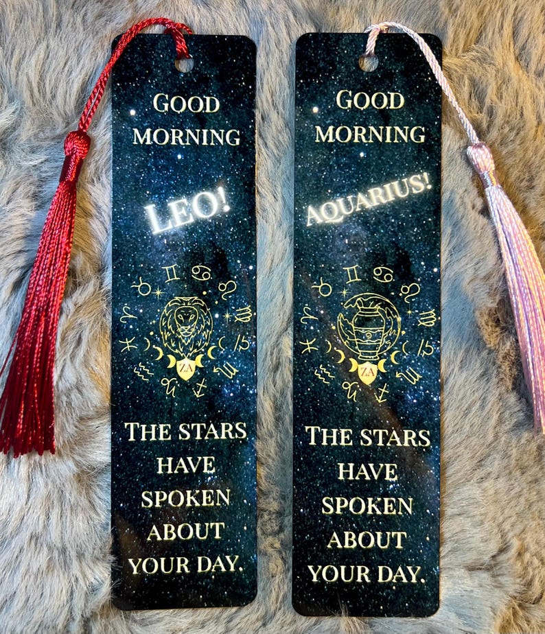 May include: Two rectangular bookmarks with a starry night design. One features "Leo!" and a lion symbol, the other "Aquarius!" and a water bearer symbol. Both have the text "Good Morning" and "The stars have spoken about your day."