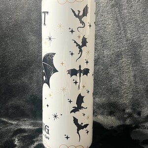 Op de afbeelding: Een witte beker met een ontwerp van zwarte draken, sterren en het woord "NIGHT" in een gestileerd lettertype. Het ontwerp bevat gouden accenten en een decoratieve rand. De beker is cilindrisch.