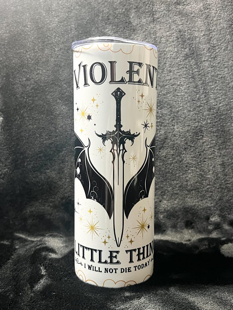 Op de afbeelding: Een witte beker met de woorden "VIOLENT LITTLE THINGS" en "I WILL NOT DIE TODAY" in zwarte letters. Het ontwerp bevat een zwart zwaard met vleermuisvleugels en gouden sterren.