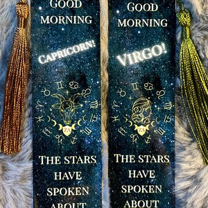 May include: Two rectangular bookmarks with a starry night sky design. One features "Capricorn!" and the other "Virgo!" with zodiac symbols. Text reads "Good Morning" and "The Stars Have Spoken About Your Day." Each has a tassel.