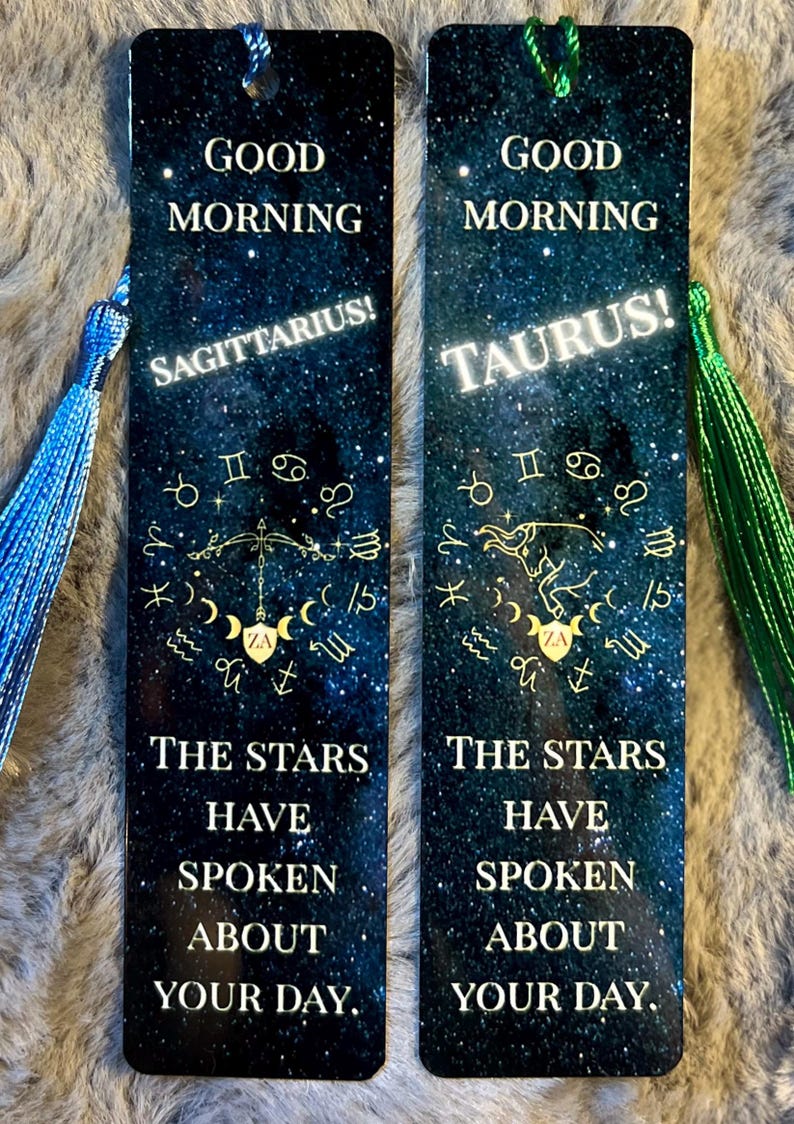 May include: Two rectangular bookmarks with a starry night sky design. One features "Sagittarius!" and the other "Taurus!" in white text. Both have gold zodiac symbols and the text "Good Morning" and "The Stars Have Spoken About Your Day."