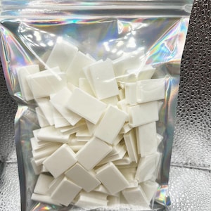 May include: A clear, iridescent zip-lock bag filled with numerous small, white rectangular foam pieces. The bag is sealed and the foam pieces are densely packed, creating a textured appearance.