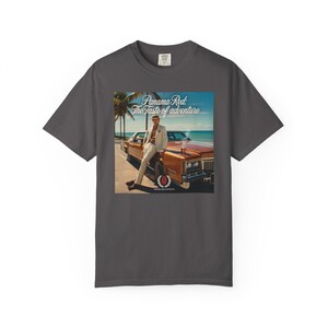 May include: Dark gray t-shirt featuring a graphic of a person leaning against a vintage orange car. The graphic includes the text "Panama Red: The Taste of adventure" in a stylized font, with a coastal backdrop.