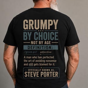 Könnte beinhalten: Ein schwarzes T-Shirt mit beigem und blauem Text auf der Rückseite, der lautet: GRUMPY BY CHOICE NOT BY AGE DEFINITION: adjective A man who has perfected the art of avoiding nonsense and still gets blamed for it. OFFICIALLY KNOWN AS: STEVE PORTER.