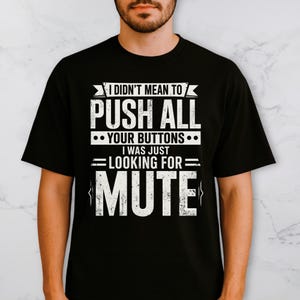 May include: Black t-shirt with white text: "I DIDN'T MEAN TO PUSH ALL YOUR BUTTONS I WAS JUST LOOKING FOR MUTE." The text is in a bold, blocky font. The shirt has short sleeves and a crew neck.