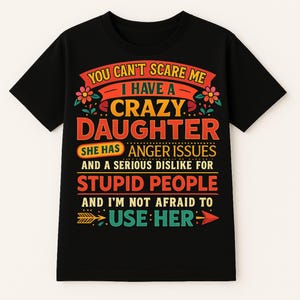 May include: A black short-sleeved t-shirt featuring a multi-colored graphic print with the text: YOU CAN'T SCARE ME I HAVE A CRAZY DAUGHTER SHE HAS ANGER ISSUES AND A SERIOUS DISLIKE FOR STUPID PEOPLE AND I'M NOT AFRAID TO USE HER, accented by flowers.