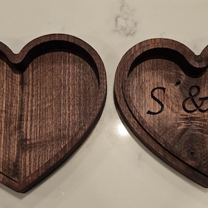 May include: Two heart-shaped wooden trays with a dark brown finish. One tray is blank, while the other has the initials "S & B" carved into the wood. The trays are likely used for decorative or functional purposes.