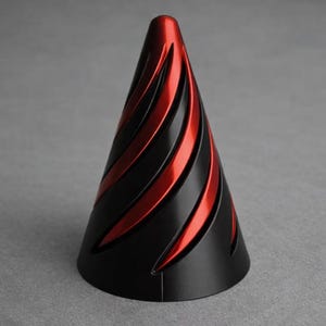 May include: A black and red decorative cone-shaped object. The cone has a matte black base and is adorned with vibrant red, curved stripes that spiral upwards. The design is sleek and modern, suitable for home decor.