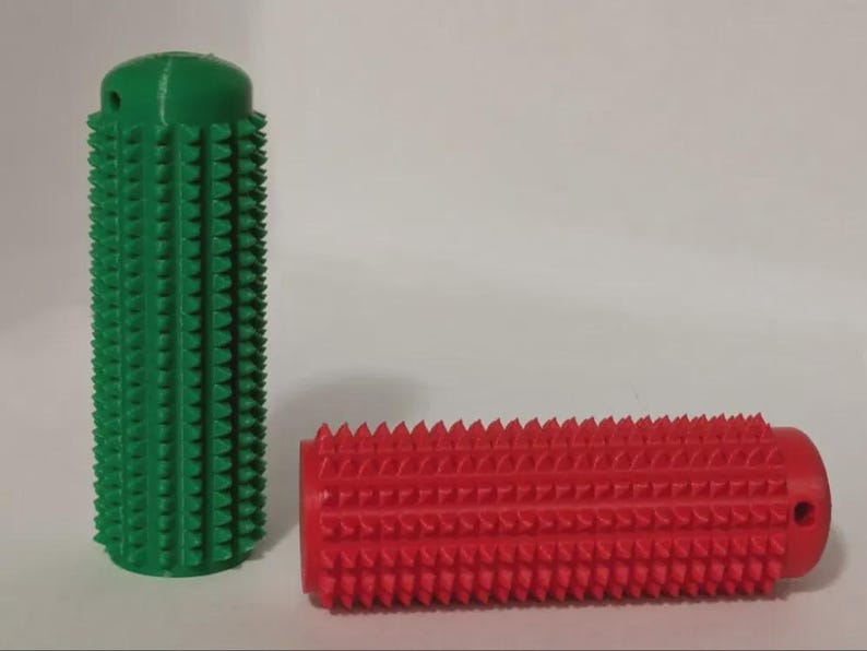 May include: Two cylindrical massage tools. One is upright and green, the other is horizontal and red. Both have a textured surface with evenly spaced, cone-shaped protrusions. The green cylinder has a small hole at the top.