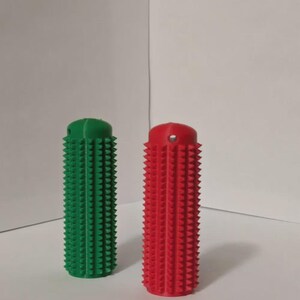 May include: Two cylindrical, textured objects. One is bright green, the other is red. Both have a series of small, conical protrusions covering their surfaces. The objects are standing upright against a plain white background.