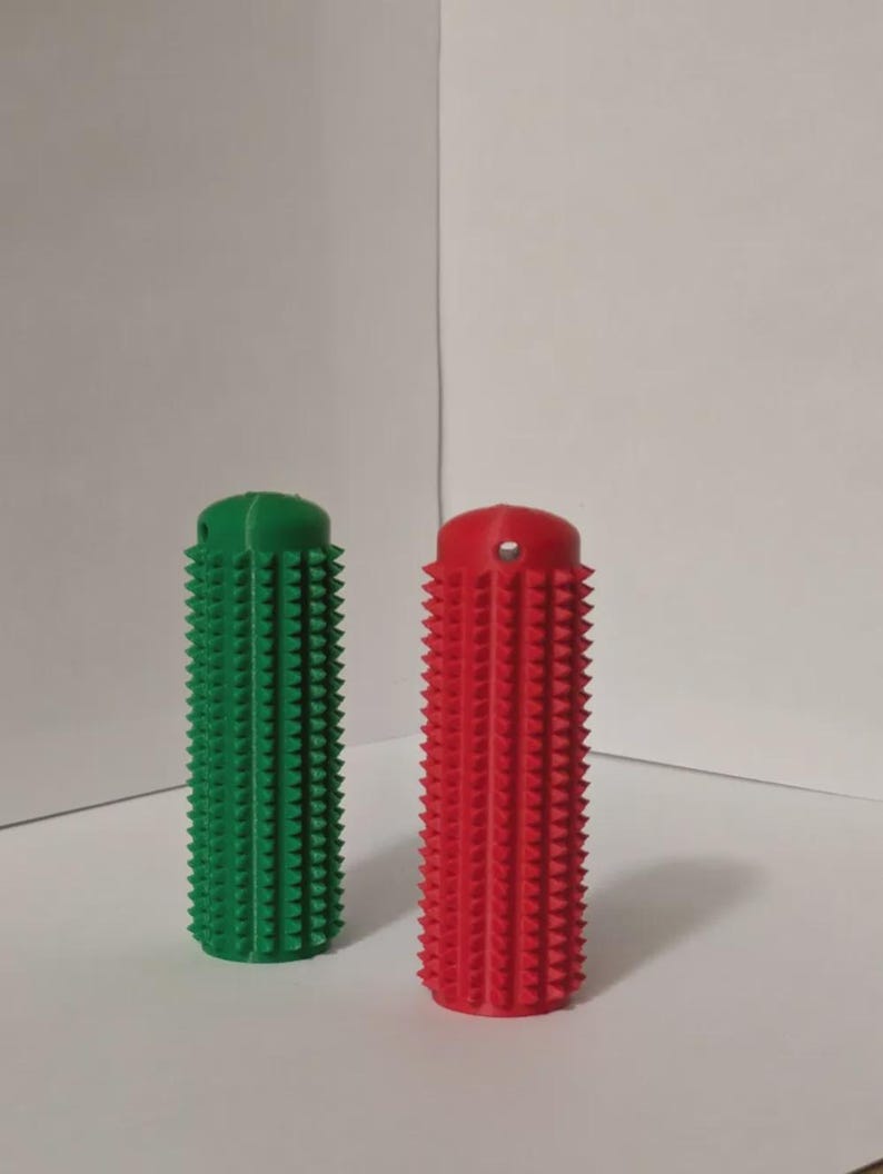 May include: Two cylindrical, textured objects. One is bright green, the other is red. Both have a series of small, conical protrusions covering their surfaces. The objects are standing upright against a plain white background.