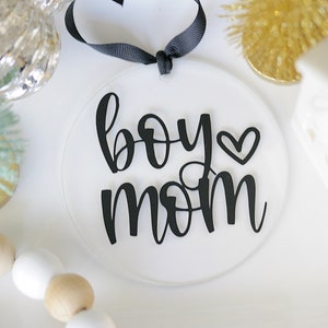 Clear 4" round acrylic ornament/tag with black vinyl reading boy mom with a heart. Hangs from black ribbon.