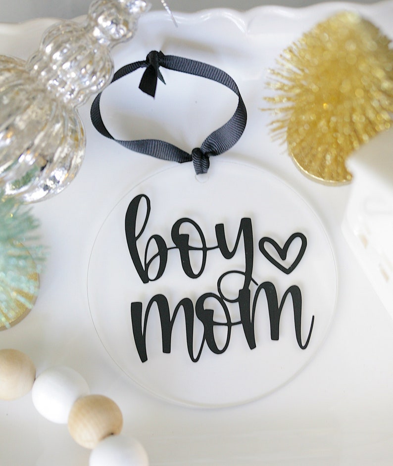 Clear 4" round acrylic ornament/tag with black vinyl reading boy mom with a heart. Hangs from black ribbon.