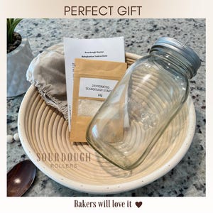 May include: A sourdough bread-making kit with a glass jar, dehydrated sourdough starter, instructions, and a proofing basket. The kit includes the text "PERFECT GIFT" and "Bakers will love it". The proofing basket is made of light-colored wood.