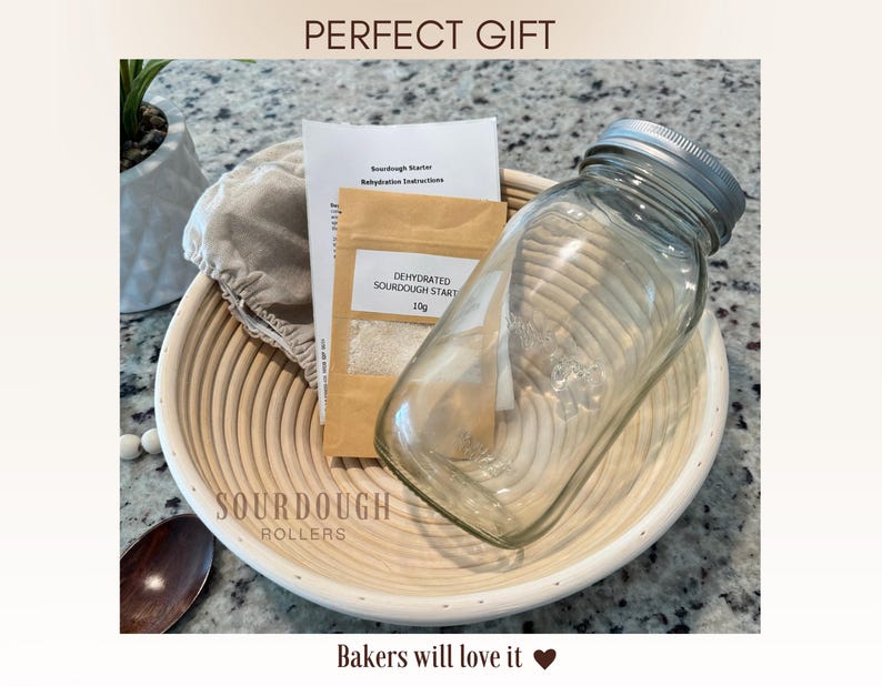 May include: A sourdough bread-making kit with a glass jar, dehydrated sourdough starter, instructions, and a proofing basket. The kit includes the text "PERFECT GIFT" and "Bakers will love it". The proofing basket is made of light-colored wood.