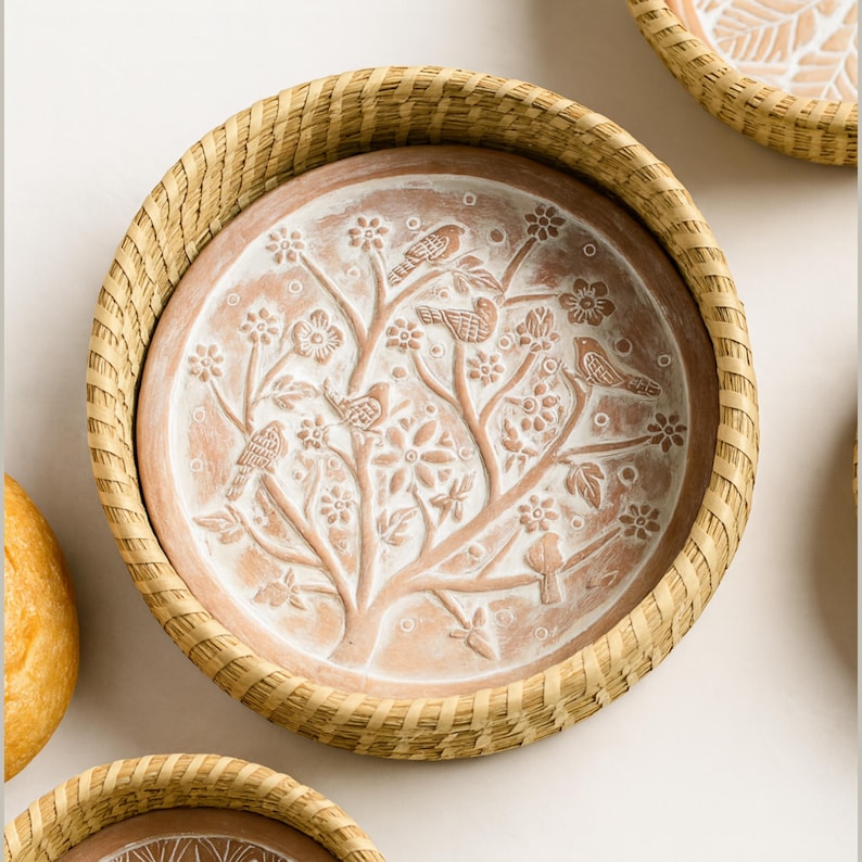 Op de afbeelding: Een ronde, terracotta-kleurige decoratieve schaal met een geweven, lichtbruine rand. De schaal heeft een reli&euml;f ontwerp van een boom met vogels en bloemen. De schaal is omgeven door een geweven, lichtbruine rand.
