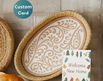May include: An oval decorative tray with a woven border and a white interior featuring a raised, swirling design in a light brown color. A greeting card with the text "Welcome New Home" is displayed in front of the tray. A blue circle with the text "Custom Card" is in the upper left.