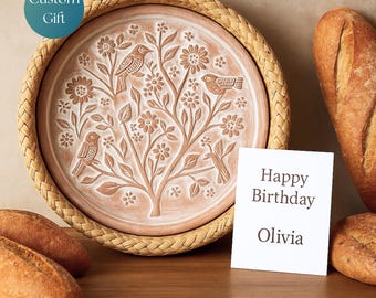 May include: A terracotta-colored decorative plate with a woven border, featuring a carved design of birds and a tree with flowers. A white card with "Happy Birthday Olivia" is next to the plate. The plate is a custom gift.