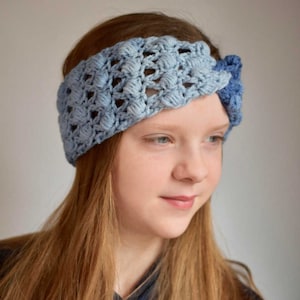 May include: A blue and light blue crocheted headband with a knot on the side. The headband is worn by a person with long, light brown hair.