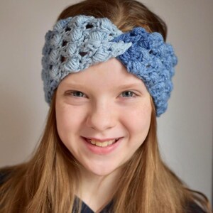 May include: A young person with long brown hair wearing a blue and light blue crocheted headband. The headband is a twisted design.