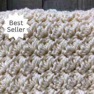 May include: Close-up of a white crocheted blanket with a textured, woven pattern. The blanket is made with a soft, fluffy yarn.