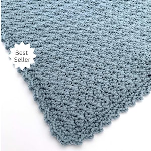 May include: A close-up of a crocheted blanket in a soft, muted blue color. The blanket has a textured surface with a repeating pattern. The edge of the blanket has a scalloped design. A white starburst graphic with the words "Best Seller" is in the corner.