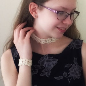May include: A woman wearing a black floral dress with a white crocheted choker and bracelet.