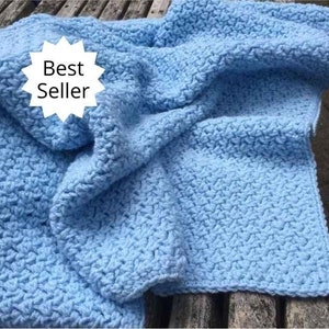 May include: A light blue crocheted blanket with a textured pattern. The blanket is folded and draped over a wooden surface. The text "Best Seller" is visible in a white starburst.