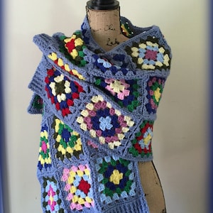 May include: A blue crocheted scarf with colorful granny squares. The scarf is draped over a mannequin.