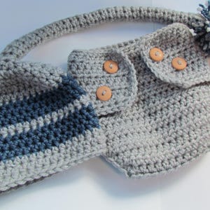 May include: A grey crocheted baby outfit with blue stripes and a matching hat. The outfit has three wooden buttons and a grey pom-pom.