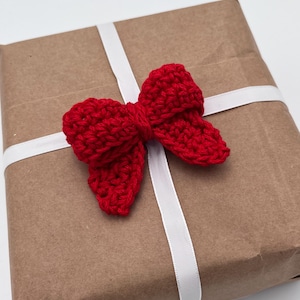 May include: A brown paper gift box with a white ribbon and a red crocheted bow.