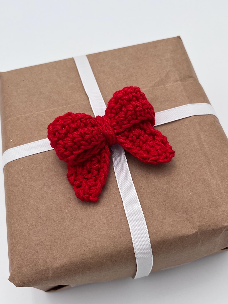 May include: A brown paper gift box with a white ribbon and a red crocheted bow.
