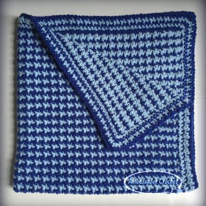 May include: A blue and light blue crocheted baby blanket with a diagonal pattern. The blanket is folded in half and the corner is visible. The blanket is made with a single crochet stitch.