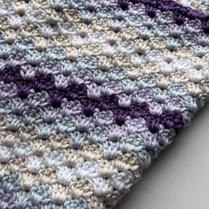 May include: A crocheted blanket with a striped pattern in shades of purple, blue, white, and beige.