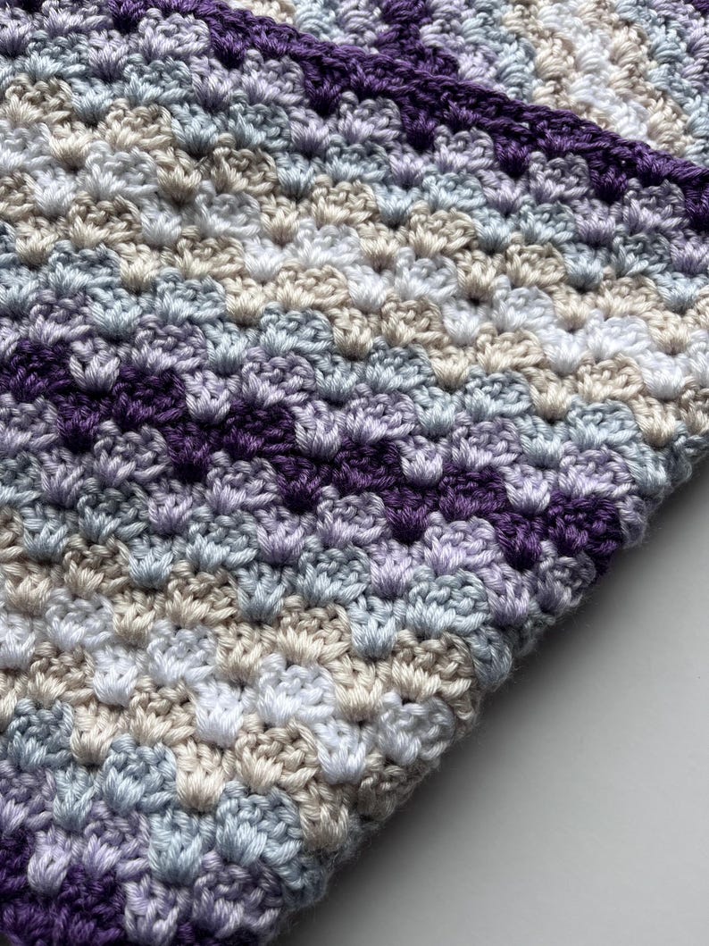May include: A crocheted blanket with a striped pattern in shades of purple, blue, white, and beige.
