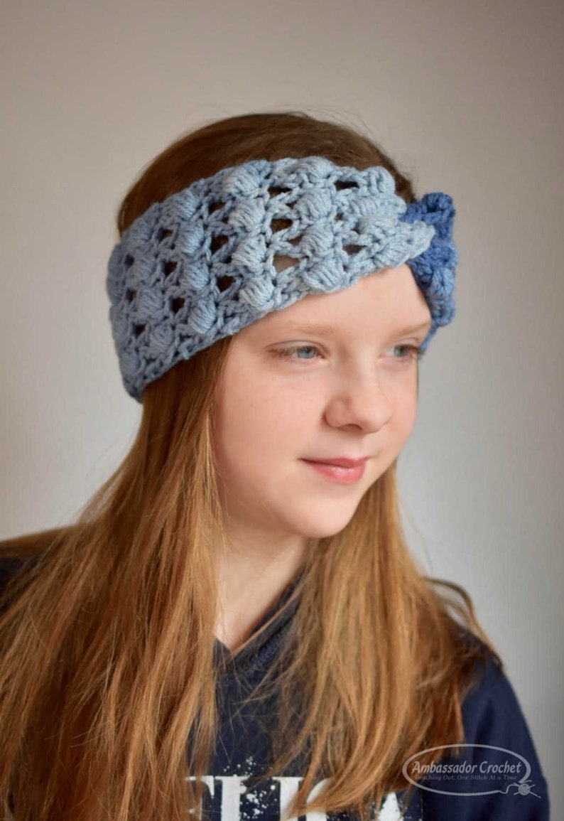 May include: A blue and light blue crocheted headband with a knot on the side. The headband is worn by a person with long, light brown hair.